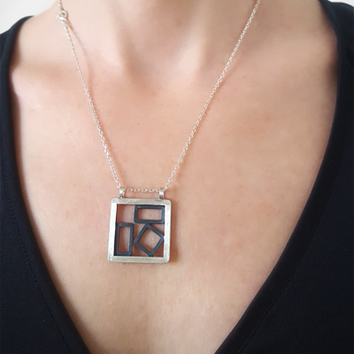 Handcrafted Geometric Patina Sterling Silver pendant is worn on the lady.