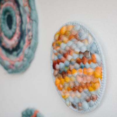 Cassandra Sabo’s ‘West Coast 2’ woven circular textile wall-hanging from her West Coast Collection hung on the wall with multiple artworks from this collection