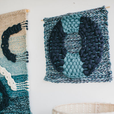 Cassandra Sabo’s ‘Flow’ handwoven textile wall-hanging from her West Coast Collection hung on the wall beside another ‘Macraweave’ wall-hanging.