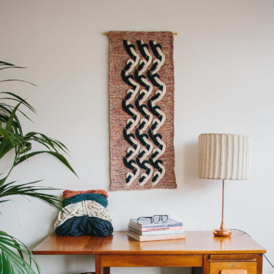 Cassandra Sabo’s ‘Elude’ handwoven textile wall-hanging from her West Coast Collection hung on the wall above a desk featuring cotton macrame cord.