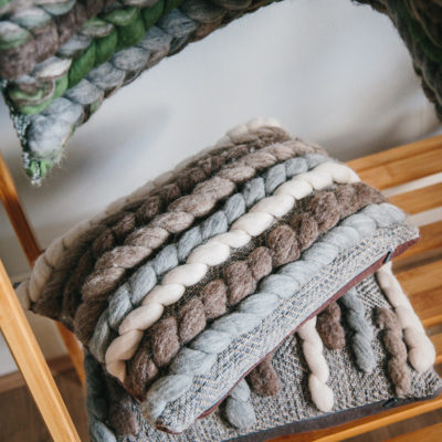 Cassandra Sabo’s handwoven wool, rectangular 'Double Tendril' cushion from her Forest Collection stacked on multiple cushions