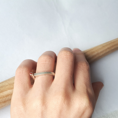 Contemporary sterling silver open ring with a round garnet is shown on the 4th finger of the palm.