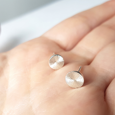 Contemporary Silver stud earrings with a sun rays texture and mirror polish on a palm.