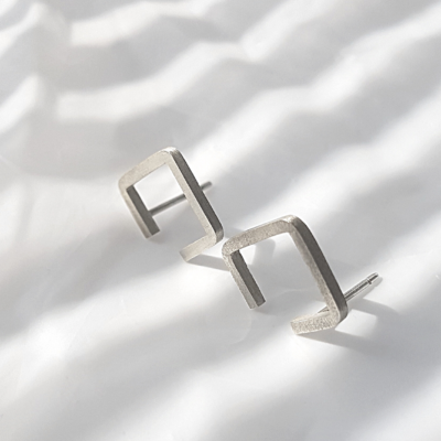 Handmade silver stud earrings on a white table.