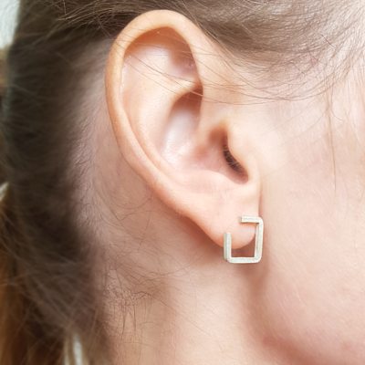 Square silver wire earrings on an earlobe.