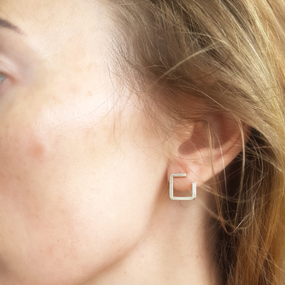 Contemporary Square silver stud earrings on an earlobe.