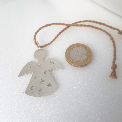 Handmade Silver Angel-Shaped Hanging Keepsake featuring a brown cotton cord and lying near a pound coin on a white surface.