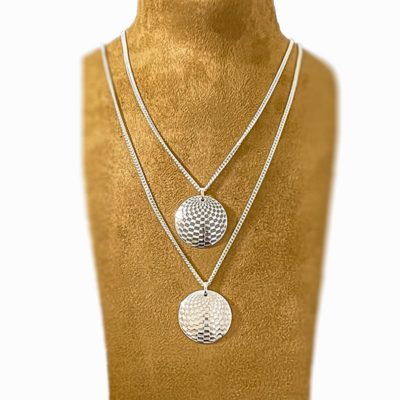 Two silver round pendant on a camel coloured suede display on a white background